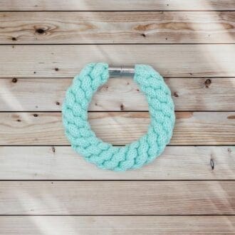 Aqua blue chunky statement bracelet made from knotted recycled cotton cord viewed from above on a light wooden background.