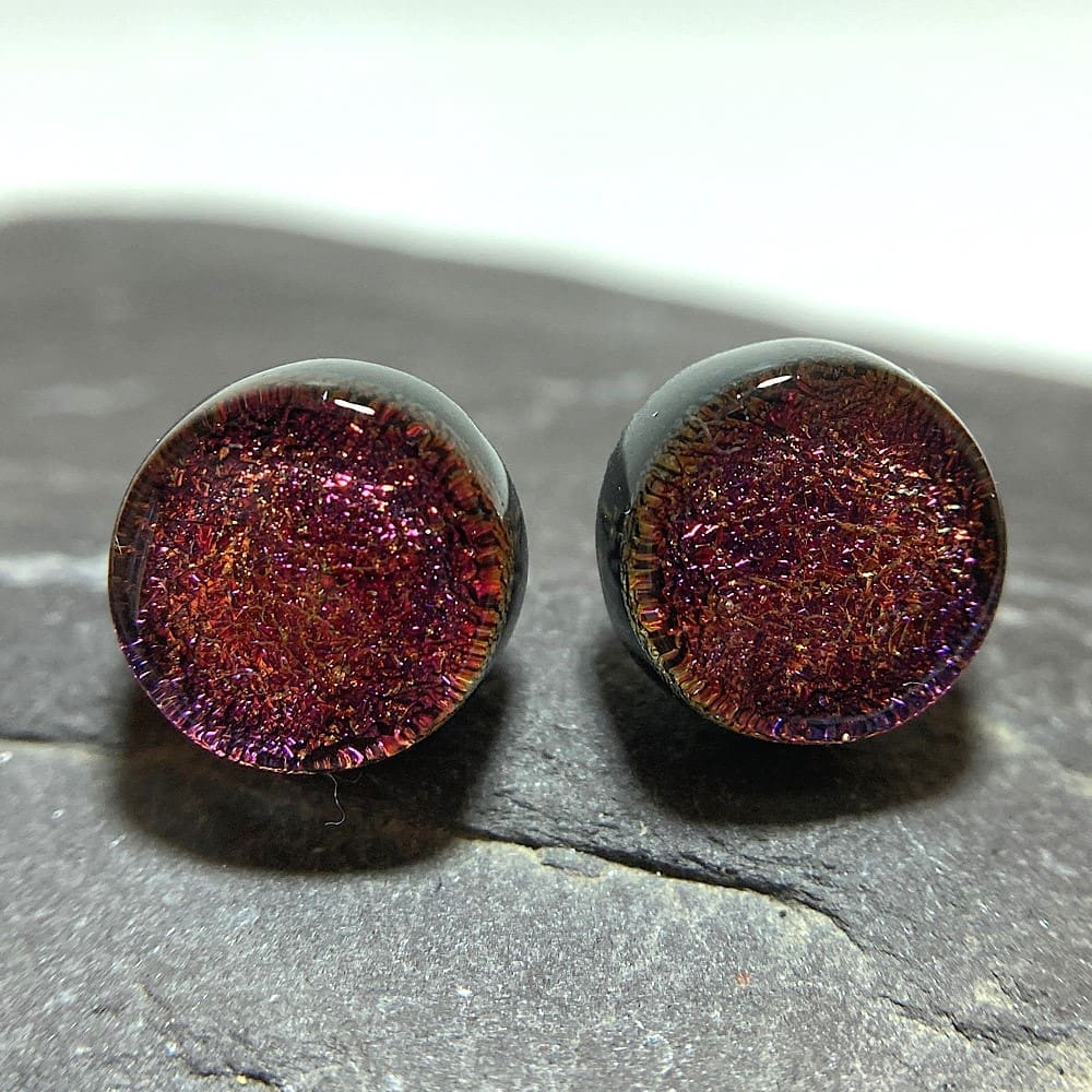A pair of cherry red fused dichroic glass stud earrings viewed from the front