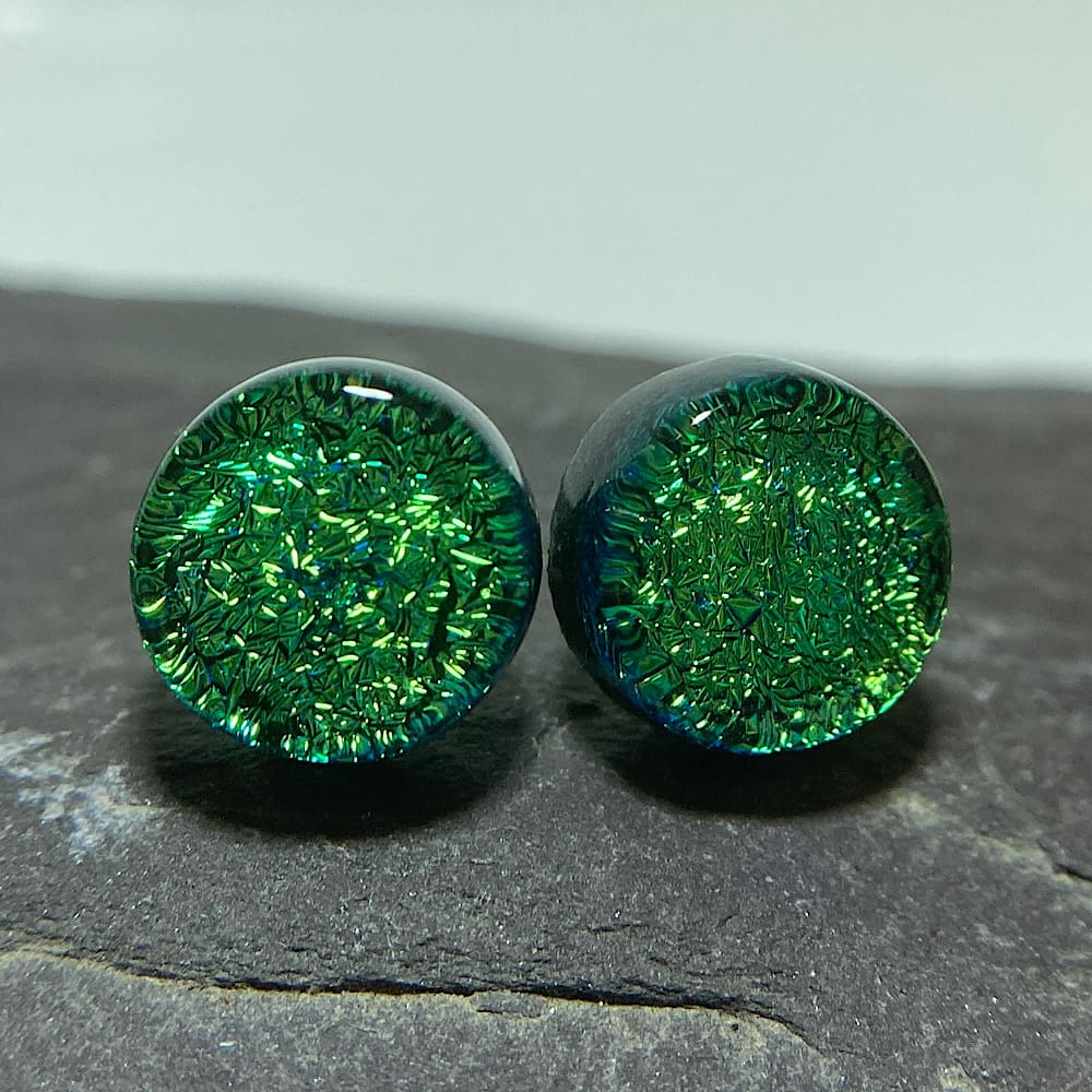 A pair of bright green fused dichroic glass stud earrings viewed from the front