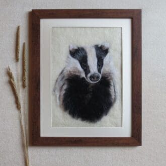 Handmade needle felted wool picture of a badger on a cream background with a dark wood effect frame.