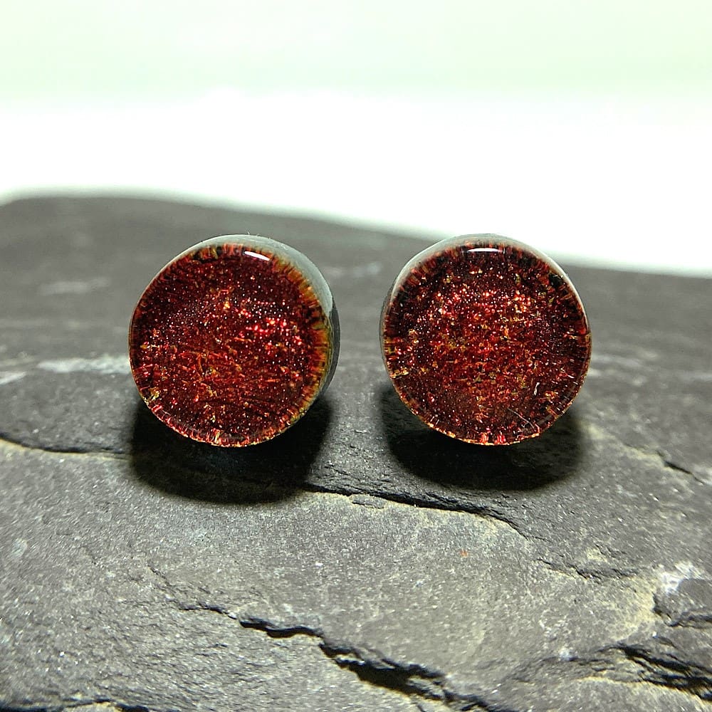 A pair of red gold fused dichroic glass stud earrings viewed from the front