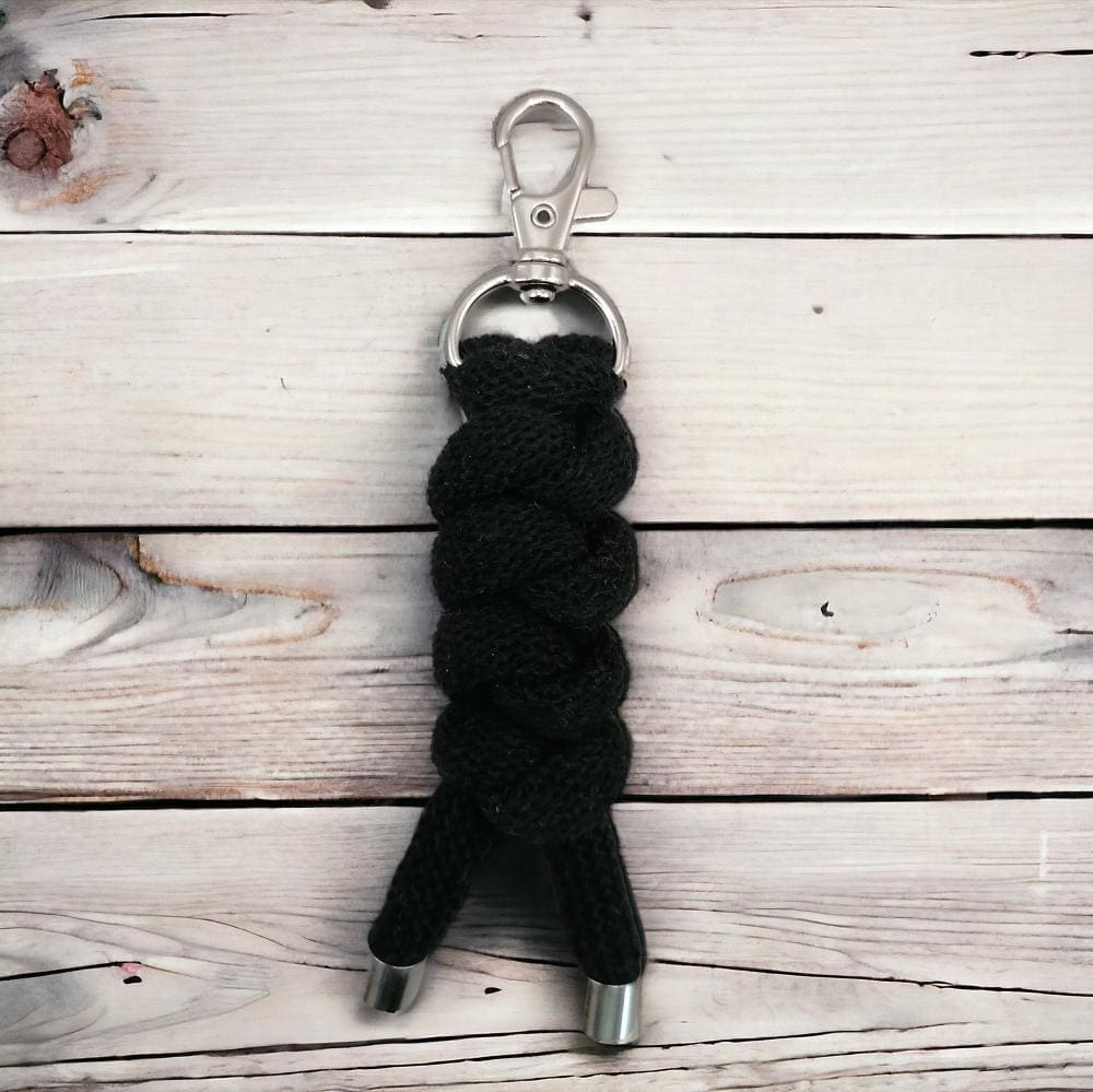 Close up of chunky black knotted cord handmade keyring that is displayed on a light wooden background.