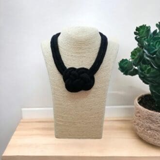 Black chunky rope necklace with central knot feature, displayed on a model that is on a light wooden counter top with a white background