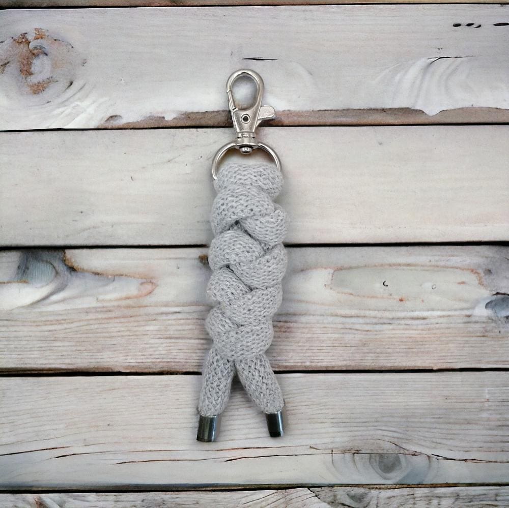 Close up of grey chunky keyring made from knotted recycled cotton cord diplayed on a a light wooden background.