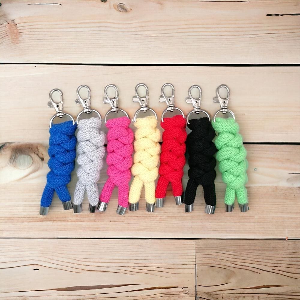 Group of colourful chunky handmade rope keyrings lined up in a row displayed on a light wooden background.