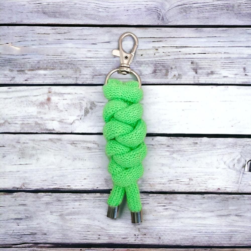 Close up of neon green chunky keyring that is made from knotted recycled cotton cord and shown on a bunch of keys that is displayed on a light wooden background.