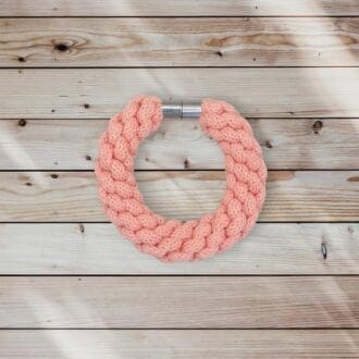 Peach chunky bracelet made from knotted recycled cotton cord viewed from above on a light wooden background.