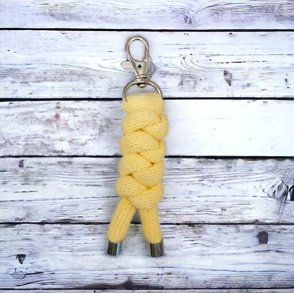 Close up of chunky yellow keyring that is made from knotted recycled cotton cord, displayed on a light wooden background.