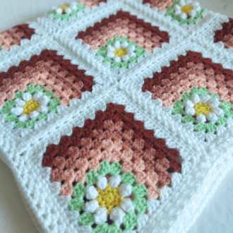 Daisy mitred granny square afghna blanket, perfect for a sofa throw or a baby blanket. Made with yellow centres and white daisy petals which are surrounded in spring green. Them shades of peach for the mitred effect. The edged in white for that clean border, and the squares have been joined in a braided design which also makes the border.
