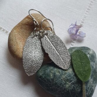 Fine silver sage leaf earrings displayed on a heart shaped stone with a real sage leaf