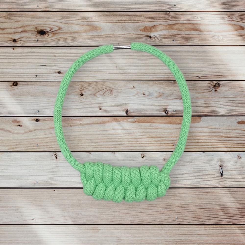 Flatlay view of neon green rope necklace with chunky knot detail, on a pine background.