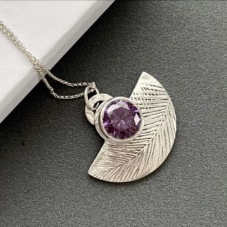 Half moon shaped fine silver necklace with a large 10mm. amethyst coloured cubic zirconia displayed on a white gift box.