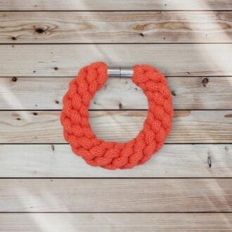 Orange chunky statement bracelet hand woven from recycled cotton cord and finished with a magnetic clasp, it is viewed from above against a light wooden background.