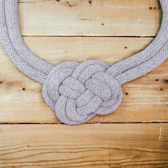 Close up of knot detail on grey rope necklace, viewed from above and displayed on a light wooden background.