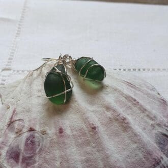 Medium 'matching' dark green sea glass nuggets wrapped in fine silver wire to create a pair of earrings, displayed on a the top of a large clam shell.