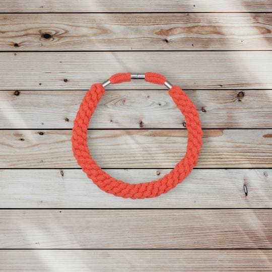 Flatlay overview image of orange chunky cord statement necklace against a light wooden background.