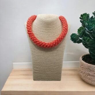 Orange chunky rope necklace displayed on a bust model that is stood on a light wooden counter top with a white background