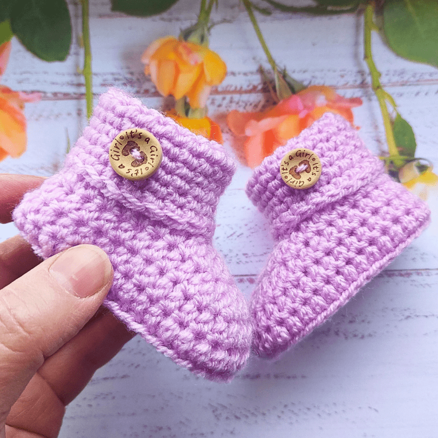 A pair of it's a girl crochet baby booties, made in pink and available in sizes newborn 0-3 and 3-6 months.