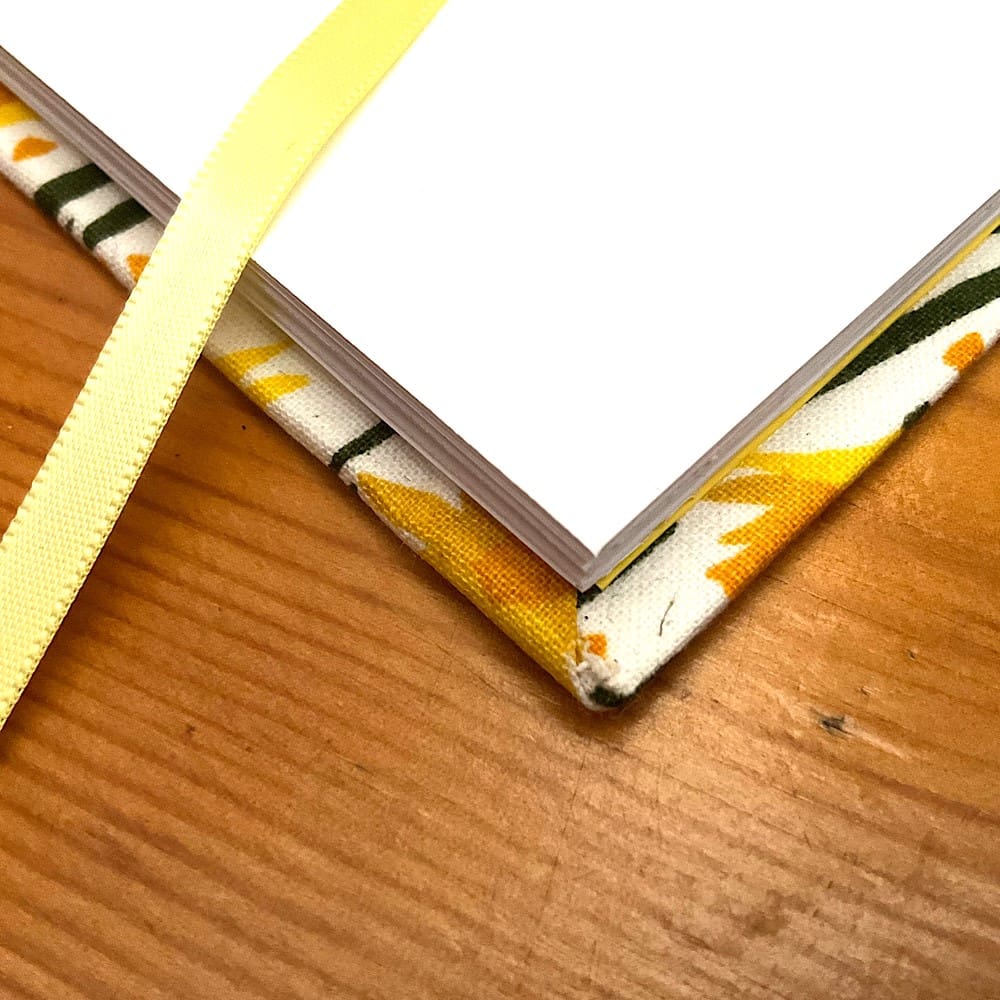 Jotter notebook filled with plain paper covered in fabric with attached pencil
