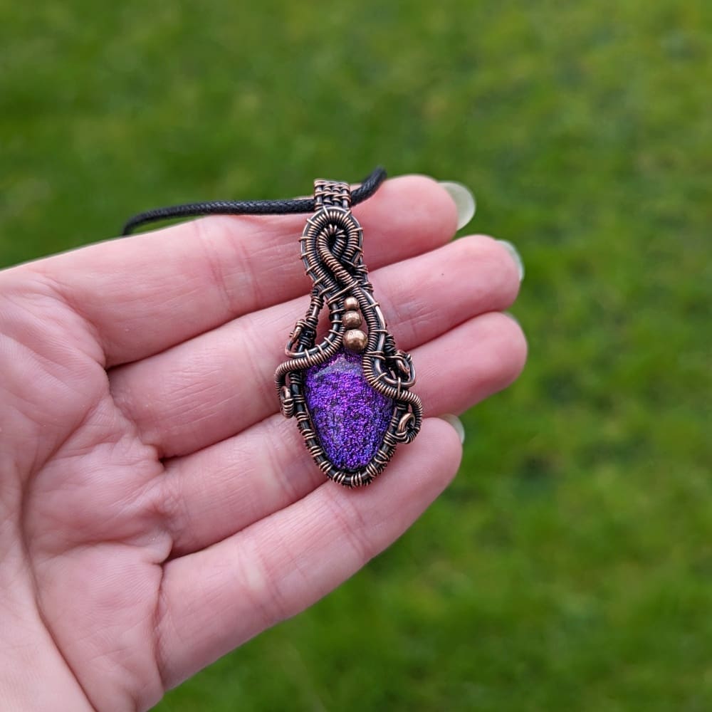 Hand holding a wire wrapped pendant with purple glass cabochon
