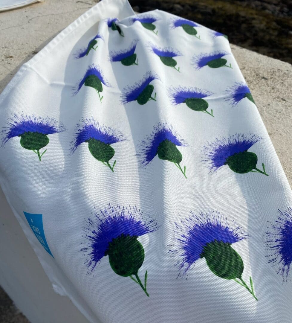 White 100% cotton tea towel printed with repeated thistle pattern