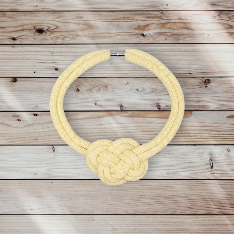 Flatlay overhead view of chunky yellow rope necklace with central knot detail displayed on a light wooden background