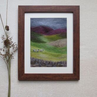A handmade wool painting of a Yorkshire Dales landscape with sheep in a field and heather on the hills.