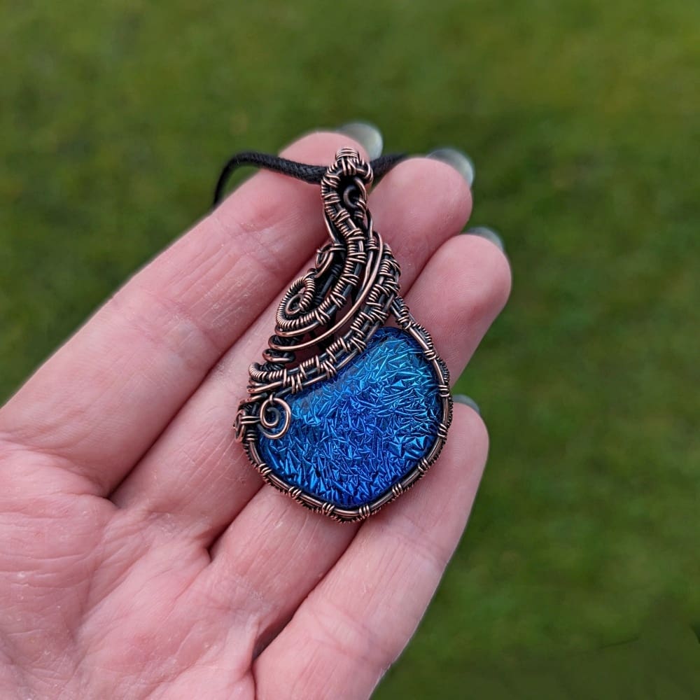 Hand holding a copper wire wrapped pendant with a blue glass cabochon