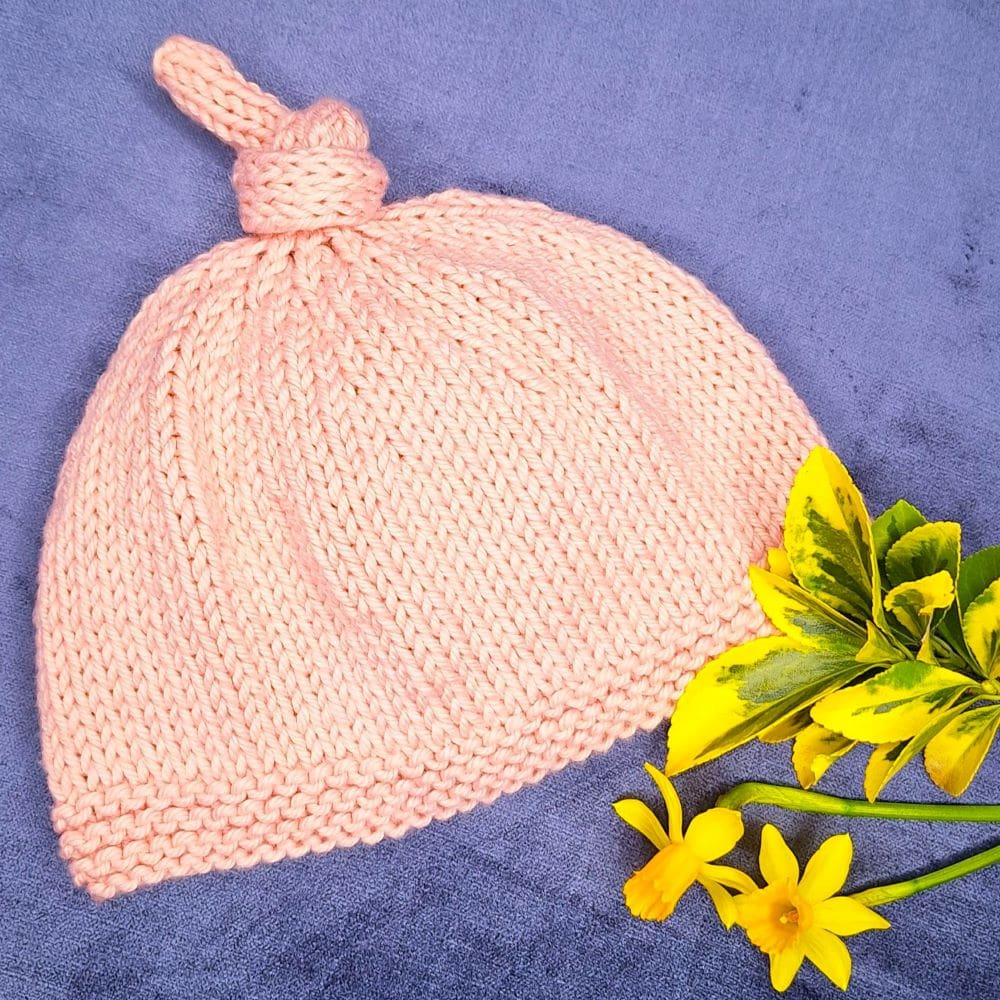 A pink 2 or 3 year old girls hat on a velvet blue background with spring flowers.
