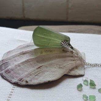A chunky pendant made of olive green sea-glass hung from a silver chain with a silver bail