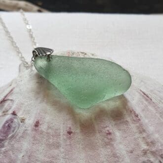 A chunky piece of sea glass in seafoam colour hung from a chain to create a stunning necklace from the sea.