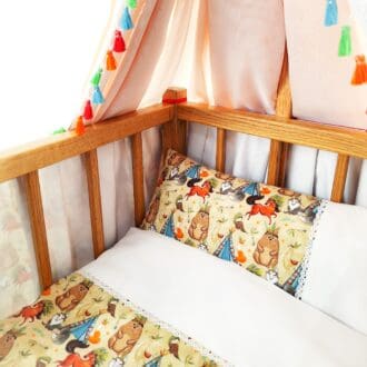 A dolls cot with bedding set in an animal theme.