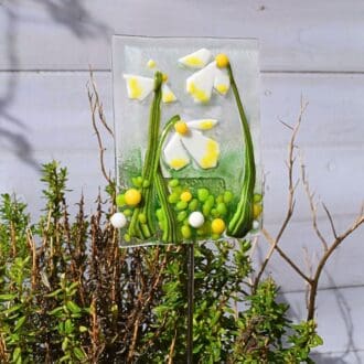 glass plant pot stake with green leaves and white and yellow flowers. Mounted on a stainless steel rod