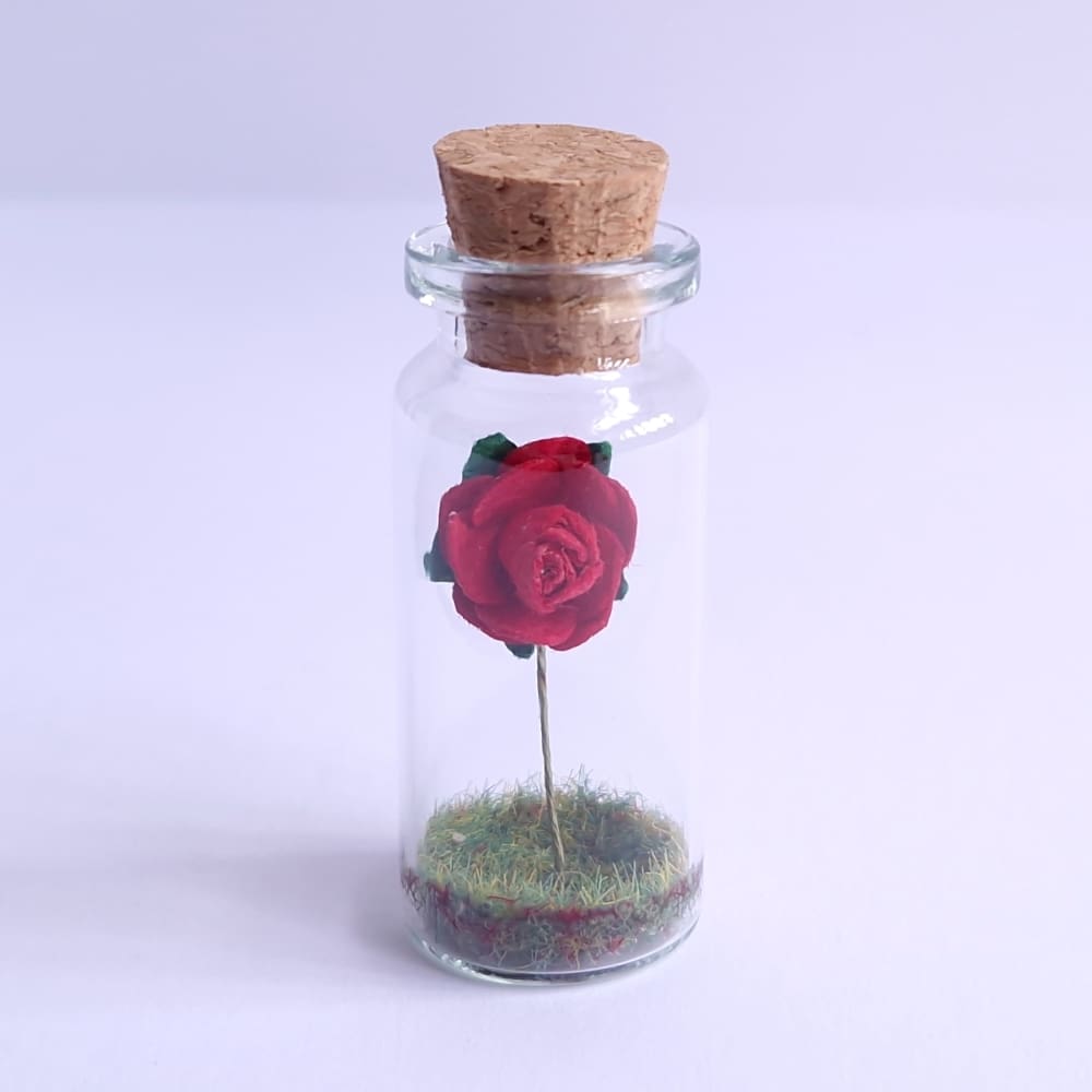 Miniature glass bottle gift with a red paper rose inside by under the blossom tree