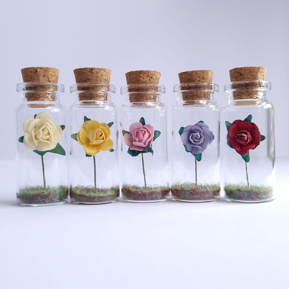 A row of different coloured paper roses in miniature glass bottles by under the blossom tree gifts