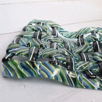 A handwoven fused glass sculpture in shades of blue, green, and white. The abstract sculpture has a wave-like form