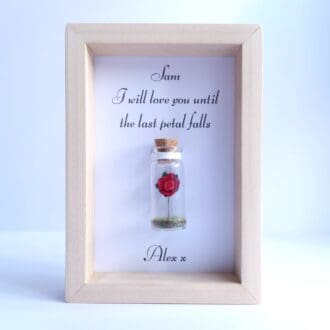 Small wooden frame with a miniature glass bottle containing a red rose in the centre.