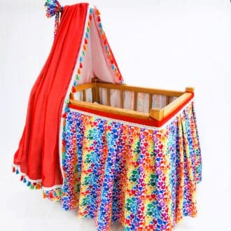 A vintage look dolls bed with canopy and decorated with colourful hearts.
