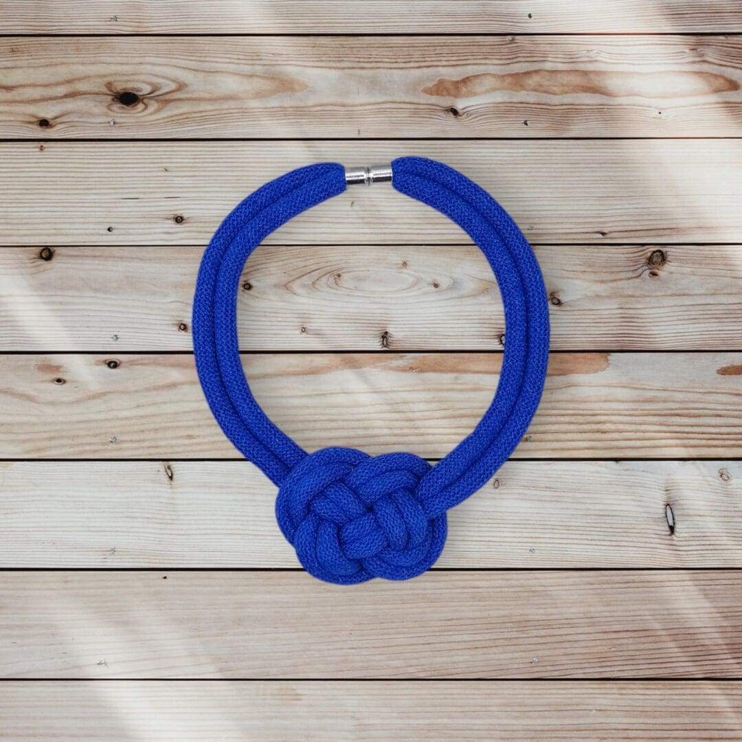 Flatlay overhead view of chunky blue rope necklace viewed against a light wood background.