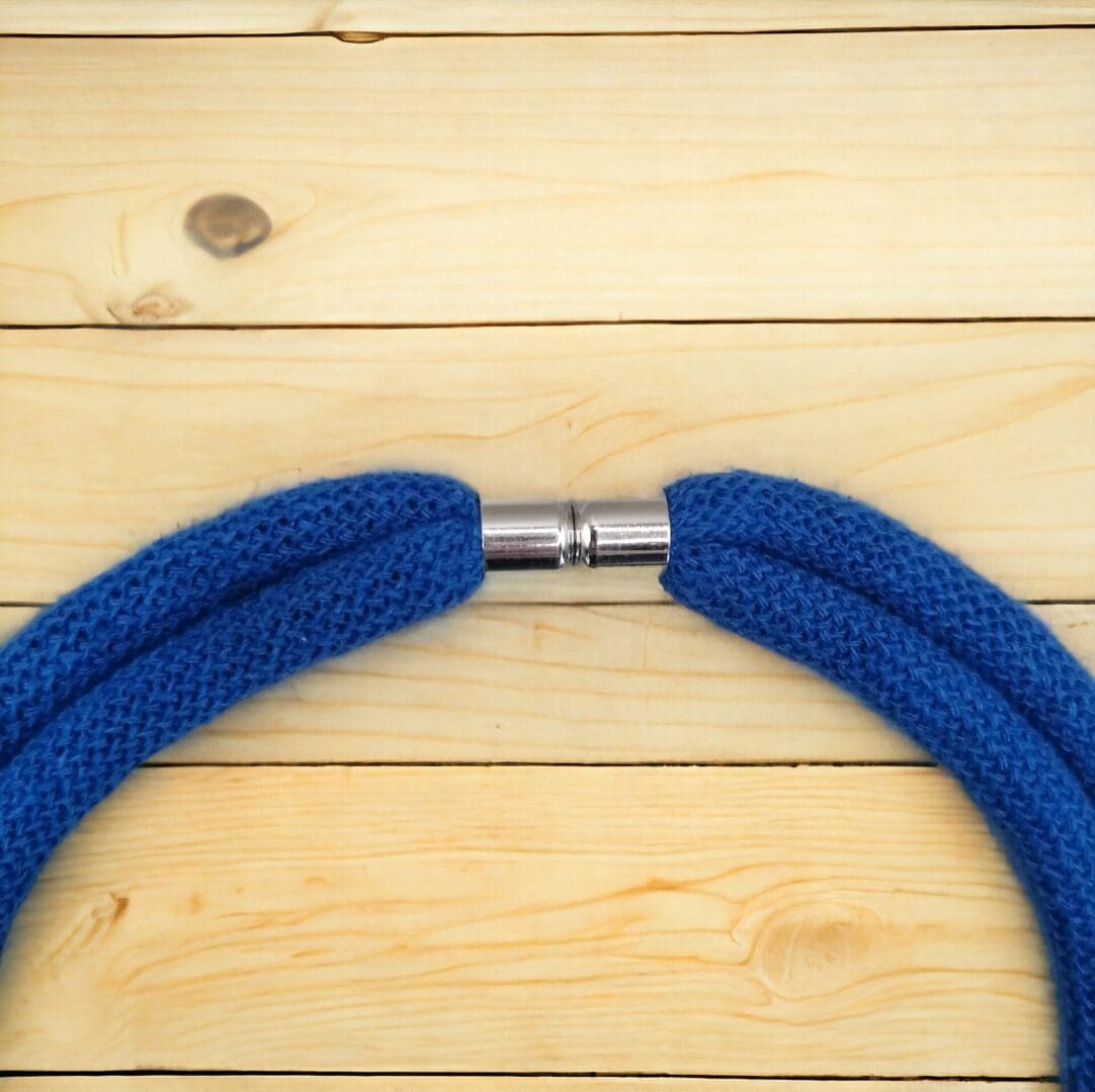 Close up of magnetic clasp on chunky blue statement rope necklace shown against a light wood background.