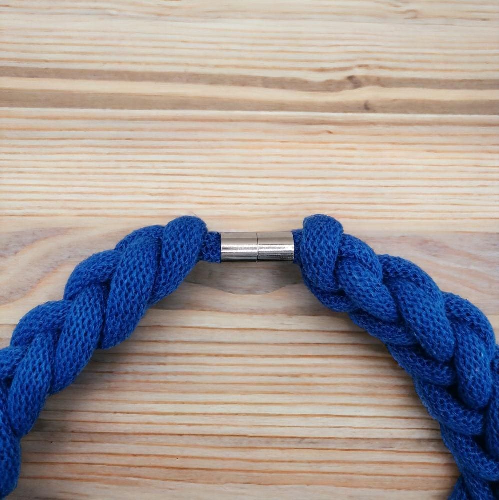 Close up of magnetic clasp detail on chunky knotted rope necklace, displayed against a light wood background