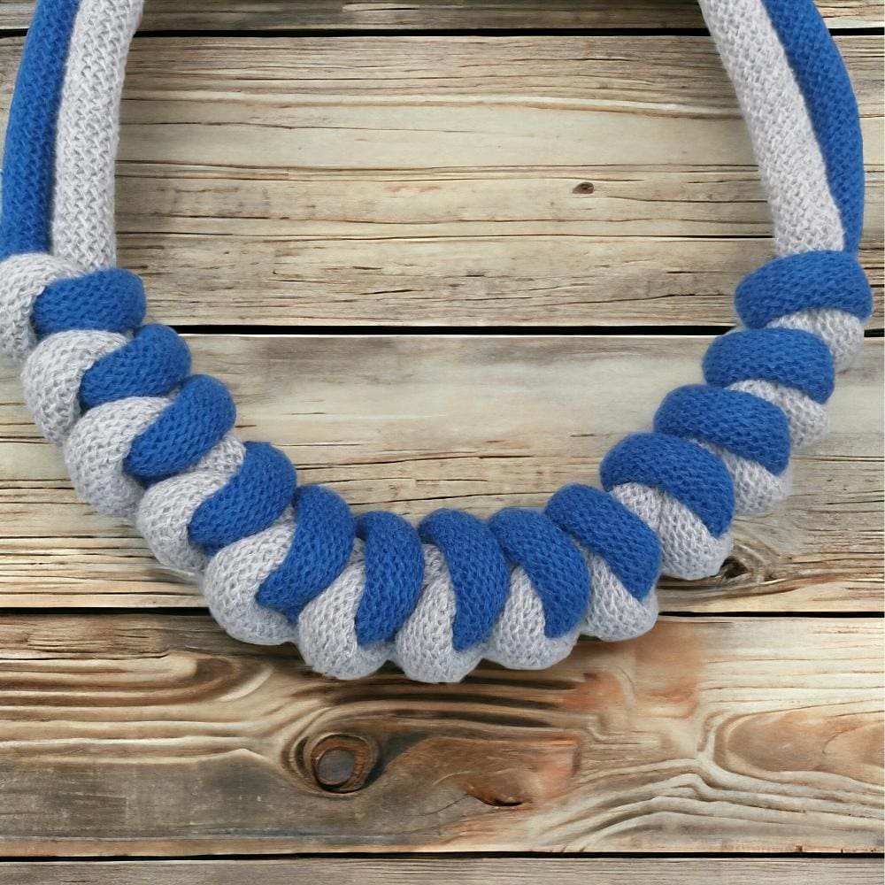 Close up of knot feature on modern chunky blue nad grey statement necklace, shown against a light wodden background.