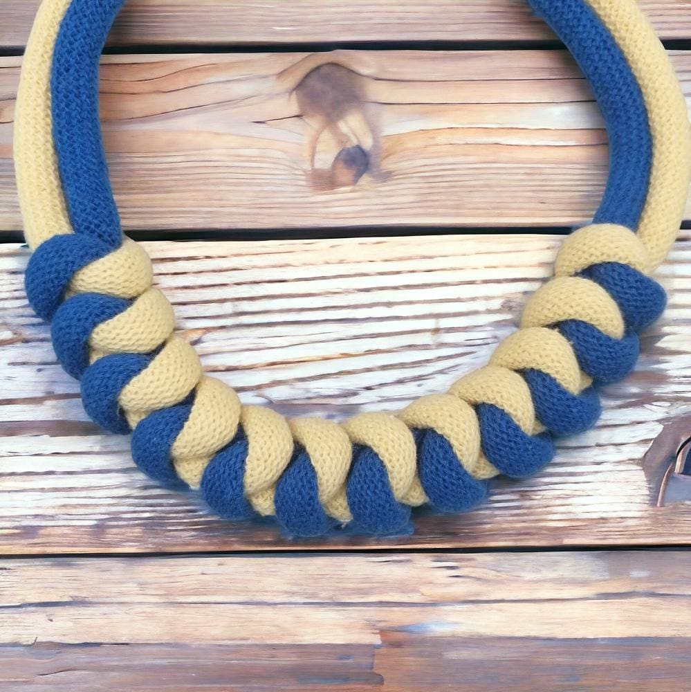 Close up of chunky knotted blue and yellow modern rope necklace shown against a light wood background
