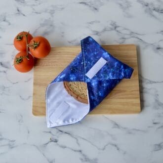 Sandwich wrap resting on a wooden chopping board, open at one end with a sandwich wrapped inside. Fabric is blue outer space themed