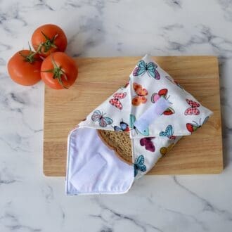 Sandwich wrap on a wooden chopping board, open at one end with a sandwich inside. Fabric is white with multi-coloured butterflies