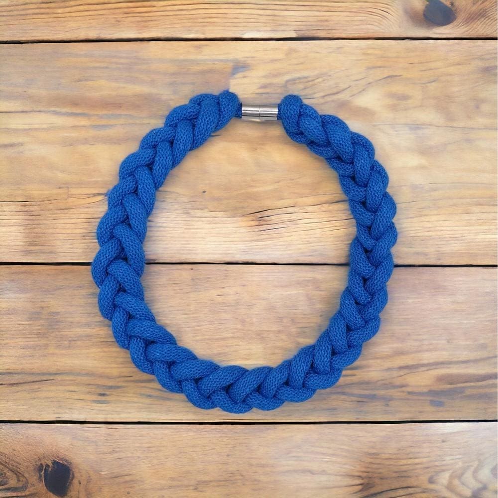 Blue chunky statement knotted rope necklace viewed from above in a flatlay style against a light wooden background