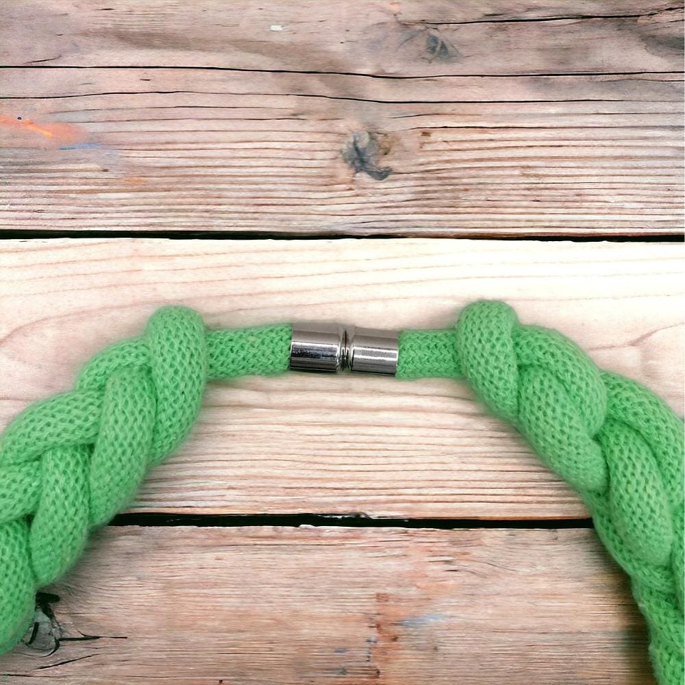 Close up of magnetic clasp detail on chunky neon green statement knotted rope necklace, shown against a light wood background