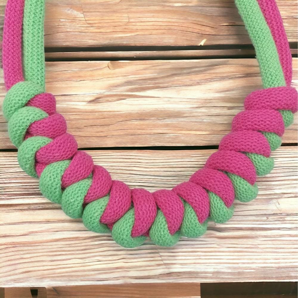 Close up of knotted pink and green modern statement necklace shown against a light wooden background.
