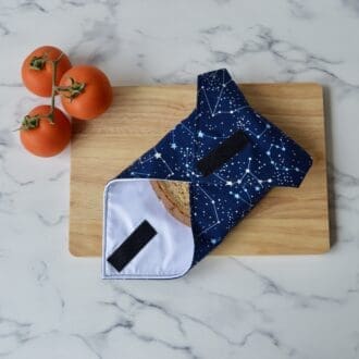 Sandwich wrap on a wooden chopping board. Wrap is open at one end with a sandwich inside. Fabric is navy with white star constellations