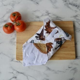 Reusable sandwich wrap on a wooden chopping board. Fabric is white with a variety of dinosaurs in natural colours